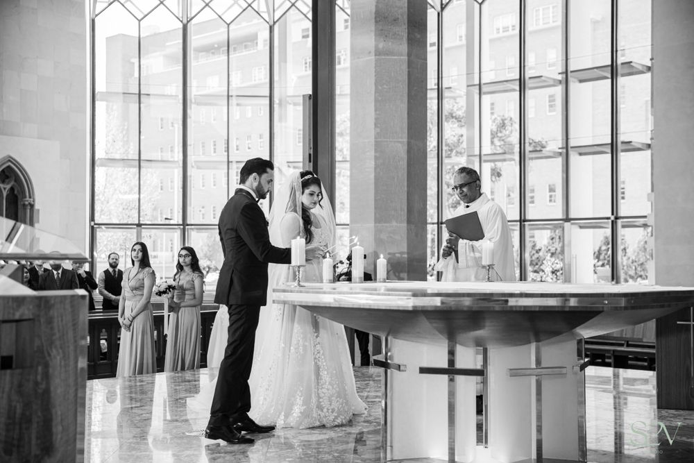 An elegant church wedding ceremony taking place beneath tall Gothic windows in black and white.