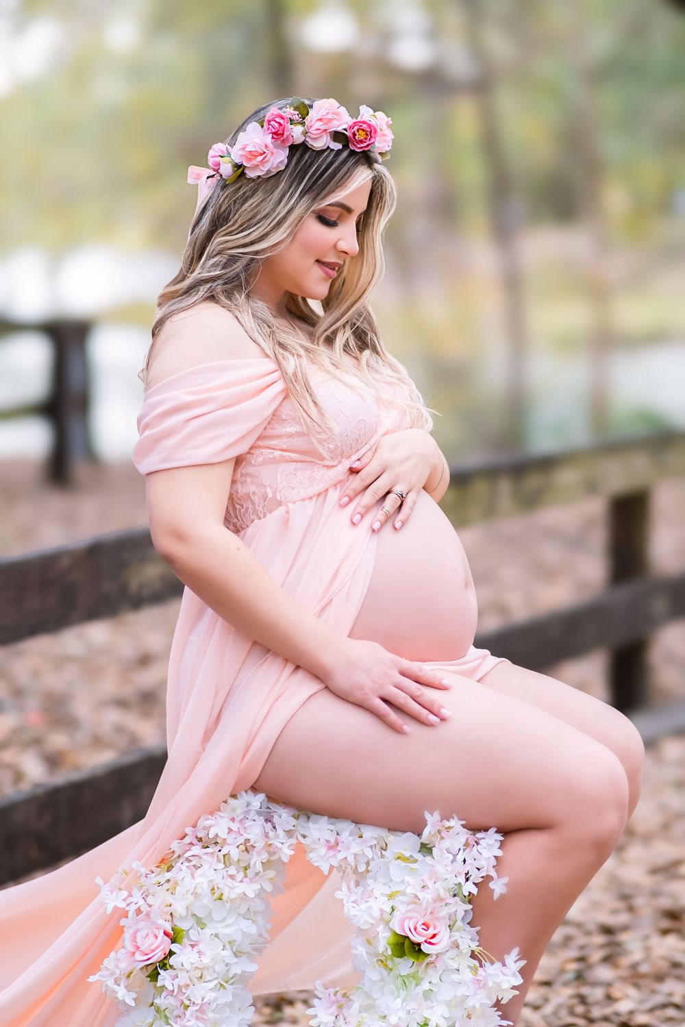 Sesión de fotos de embarazo al aire libre con vestido rosa y corona de flores, ideal para inspirar maternidad y elegancia natural.