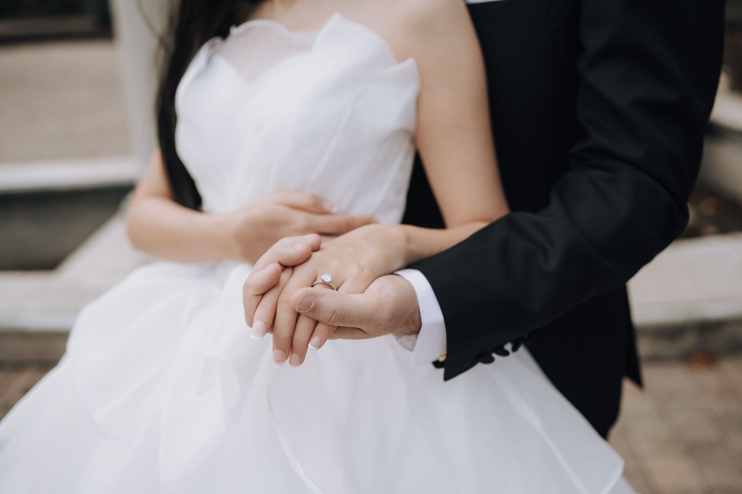 Close-up of newlyweds' hands showing off wedding rings against a white wedding dress.