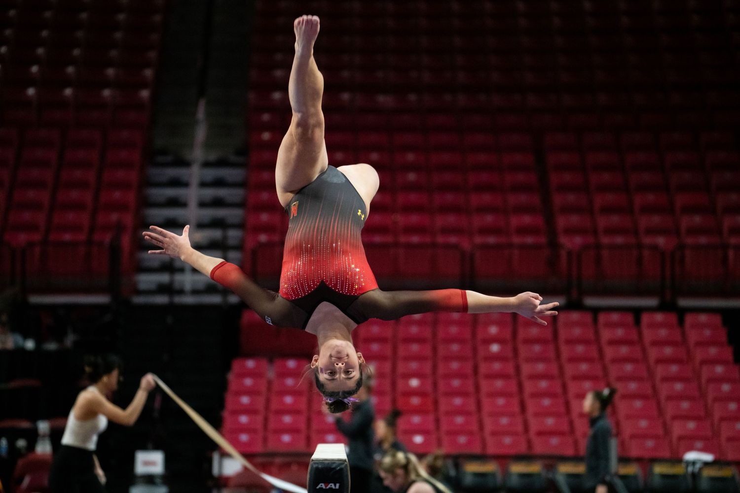 Sequence of a gymnast performing an aerial flip routine in an empty stadium with red seats.