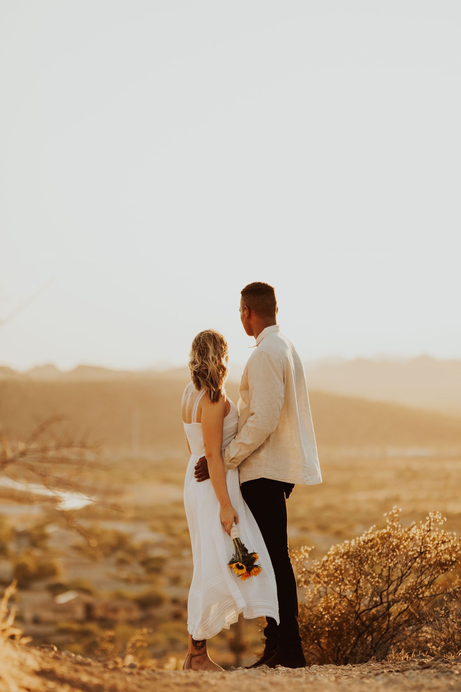 Young couple facing away from the camera overlooking a warm sunkissed desert valley
