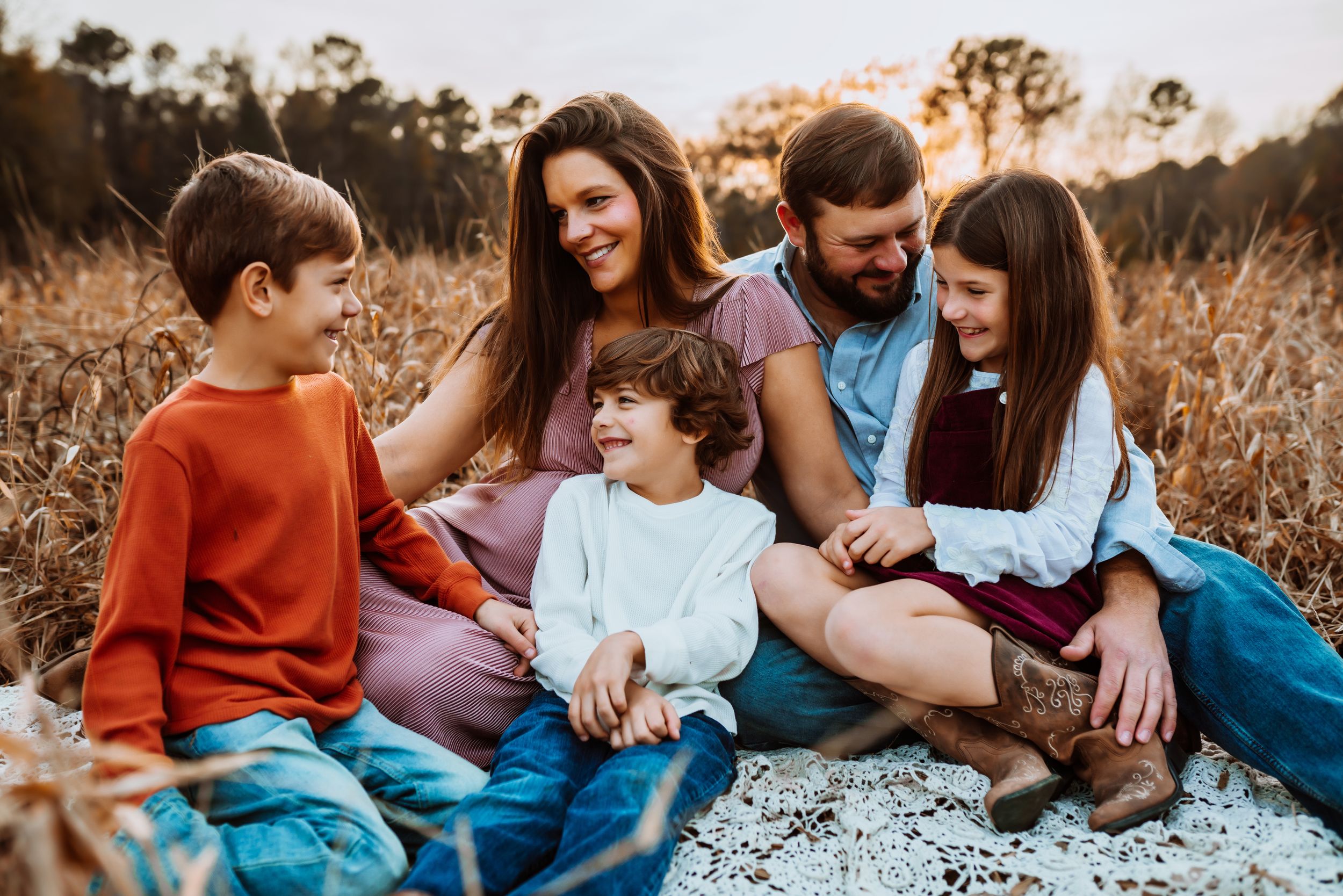 family smiling at each other in a field at sunset on a blanket