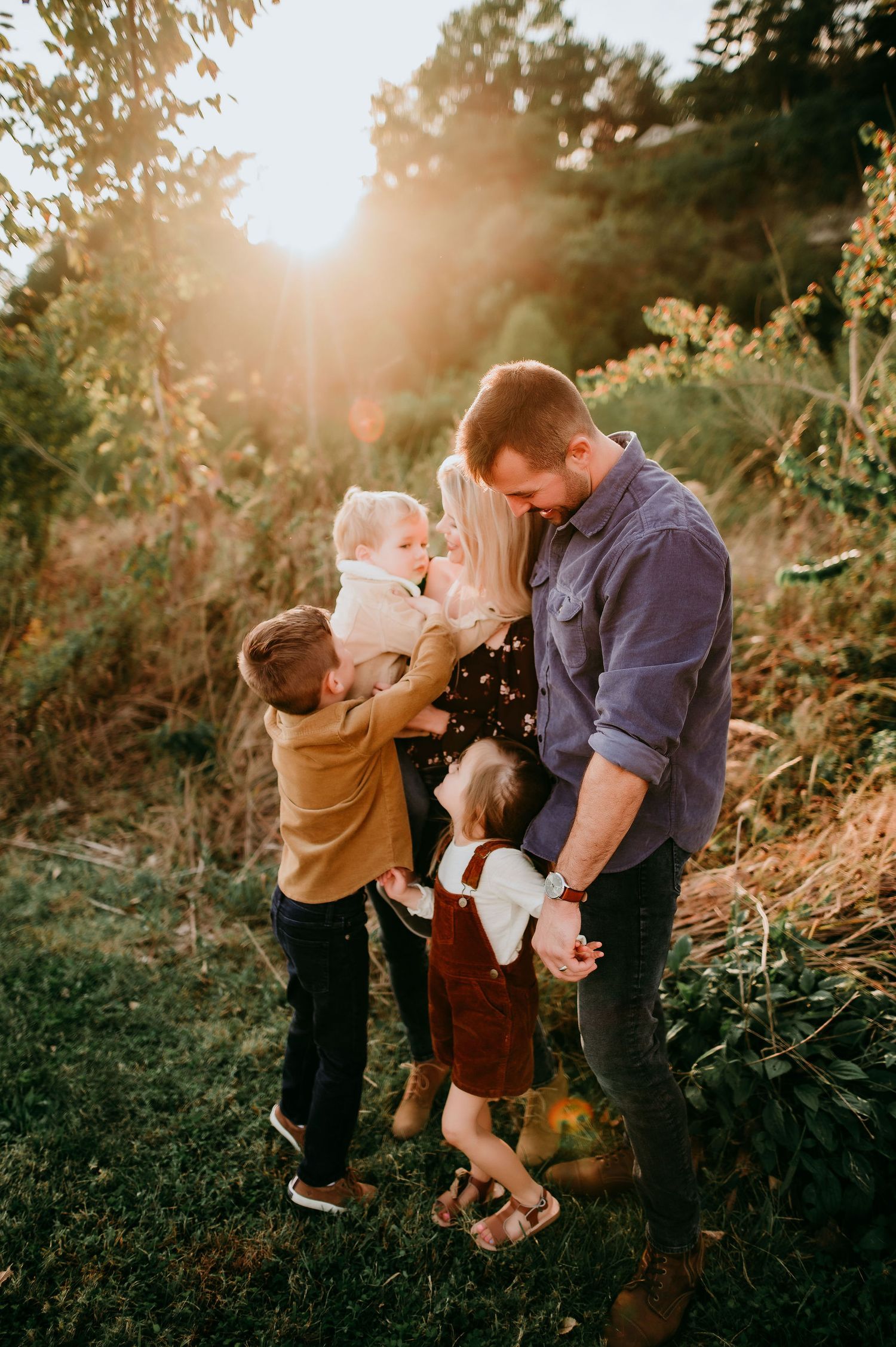 Family embraces during golden sunset in nature with beautiful backlit glow.