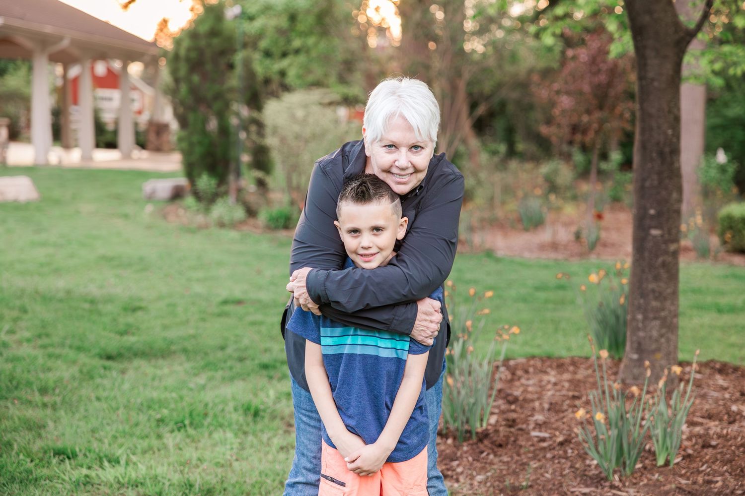 A warm embrace shared between two people outdoors with a house visible in the background.