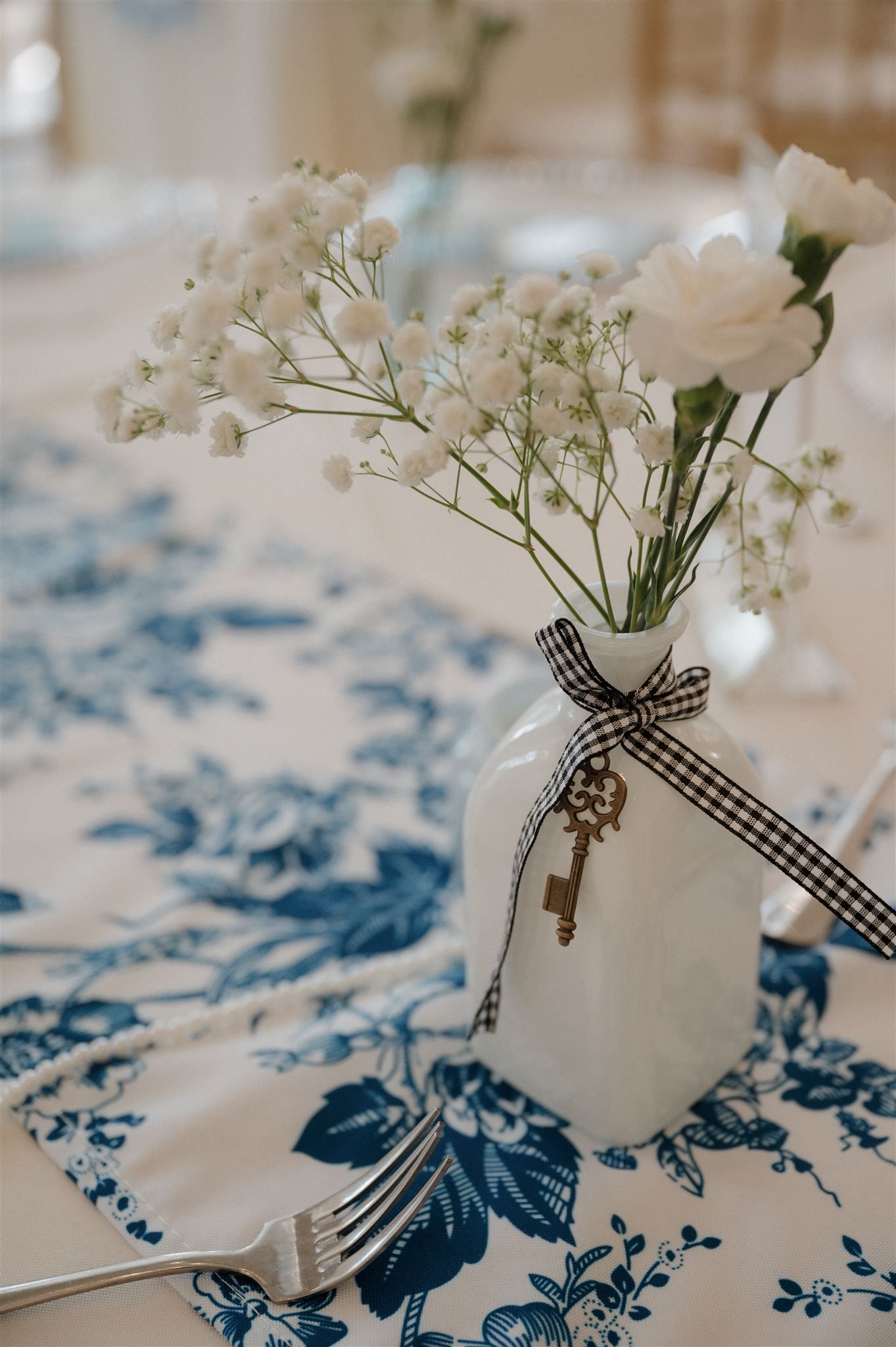 White floral arrangement with baby's breath in vase decorated with checkered ribbon and vintage key.