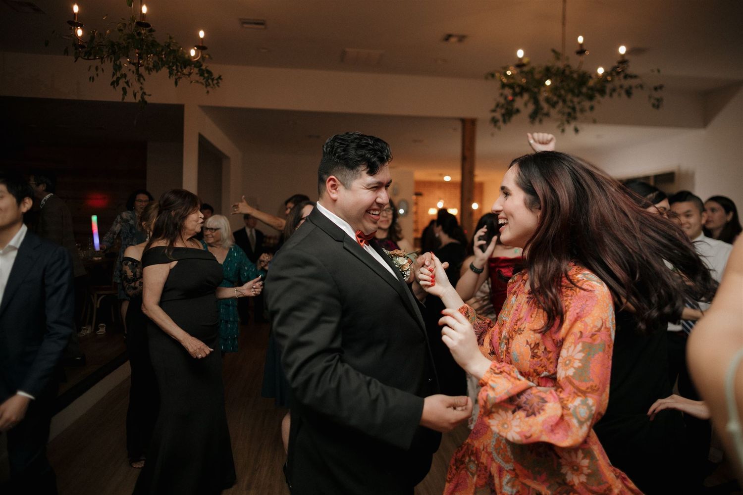 Guests dance and celebrate at a dimly lit wedding reception venue.