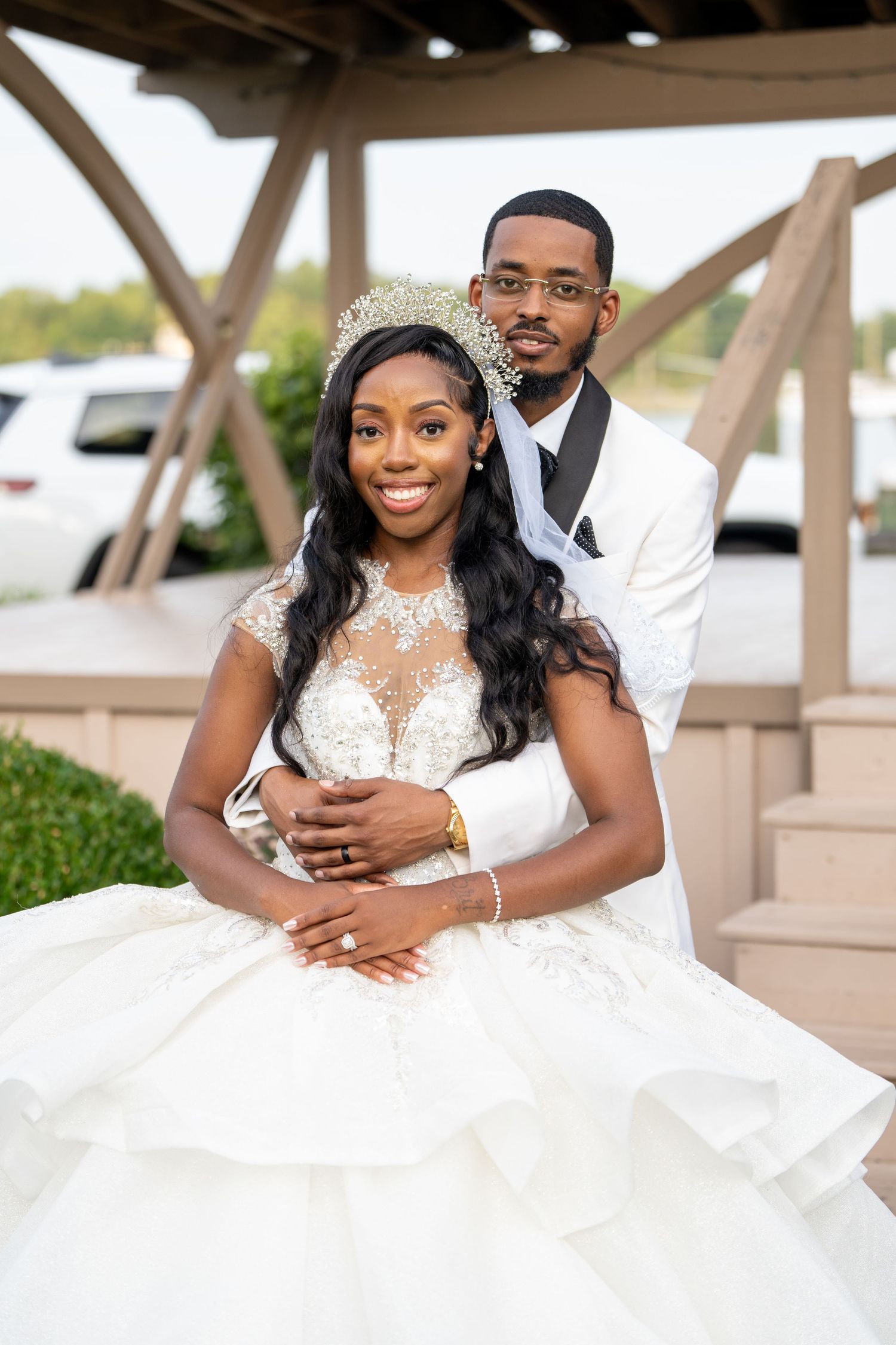 Elegant bride wearing a beaded crown and lace ball gown poses with her groom in a white tuxedo at their wedding.