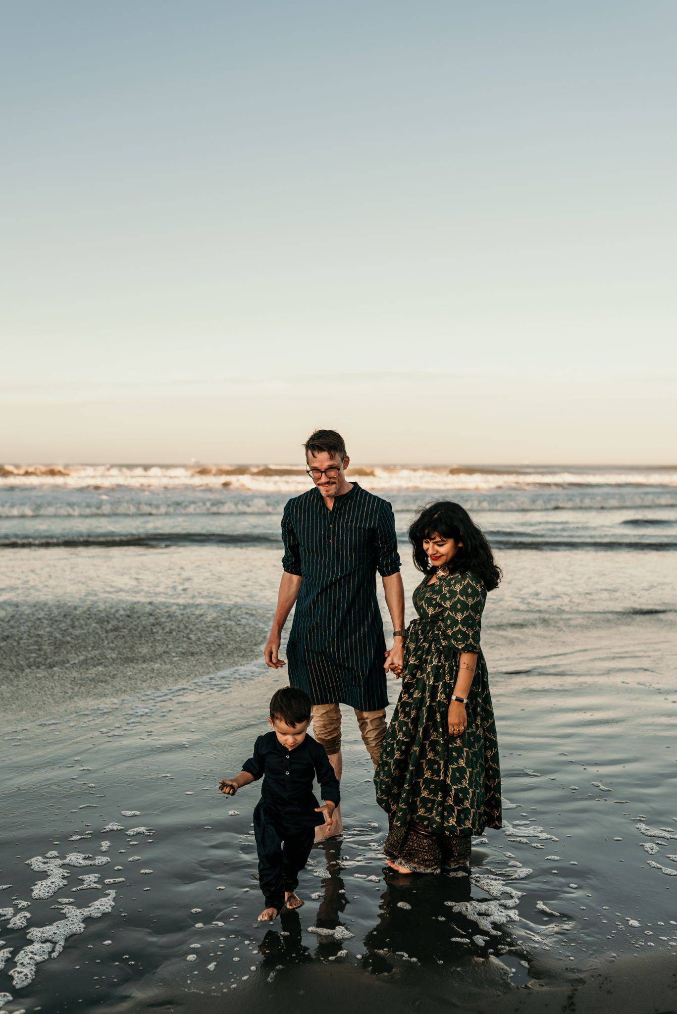 A family enjoys a peaceful moment together walking along the wet sand at the beach.