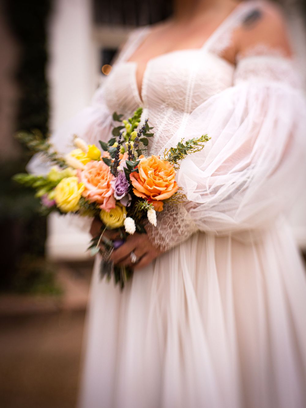 Close-up of bridal bouquet with orange and yellow roses against white dress.
