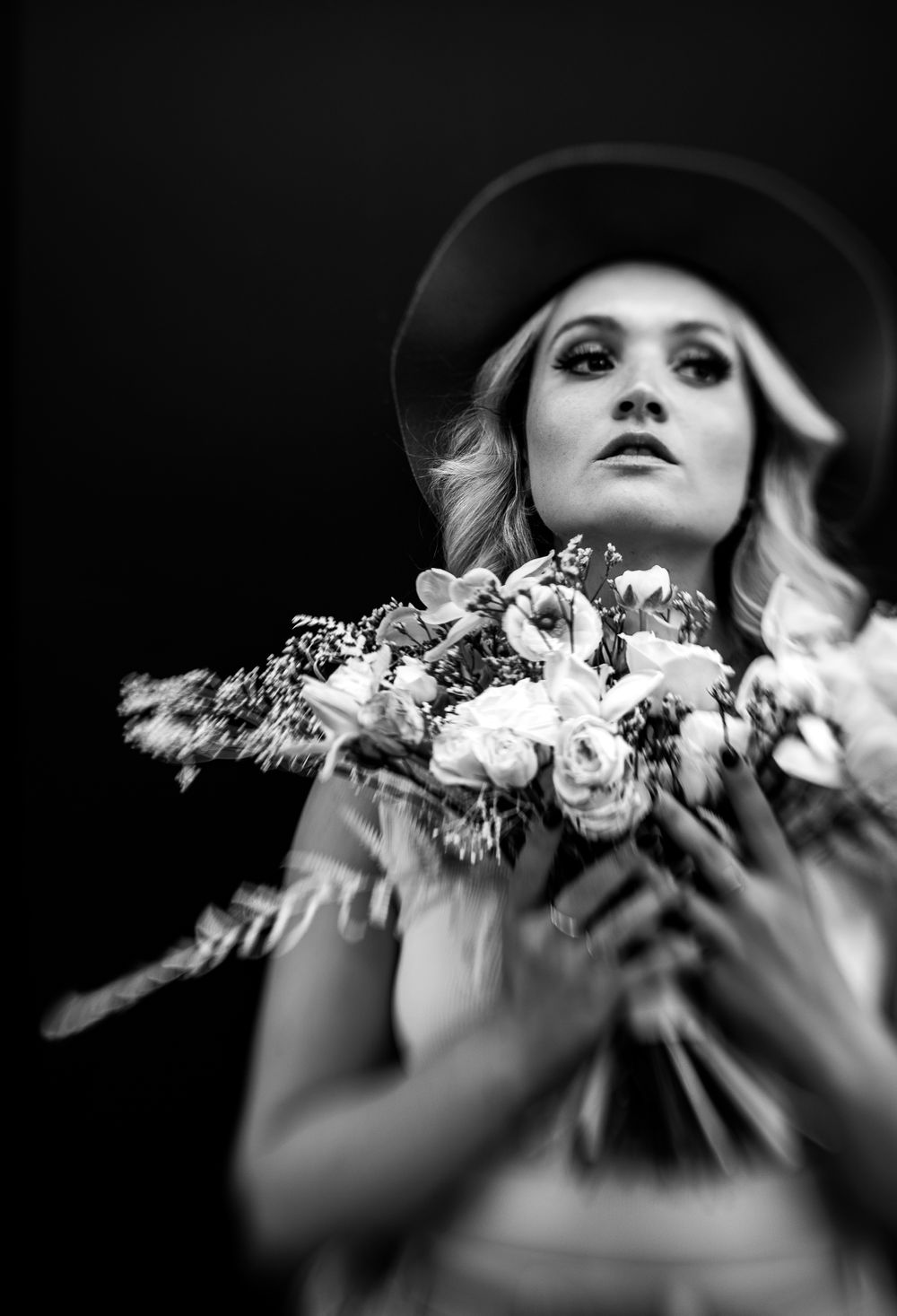 Artistic black and white portrait holding romantic bouquet of flowers while wearing a wide-brimmed hat.