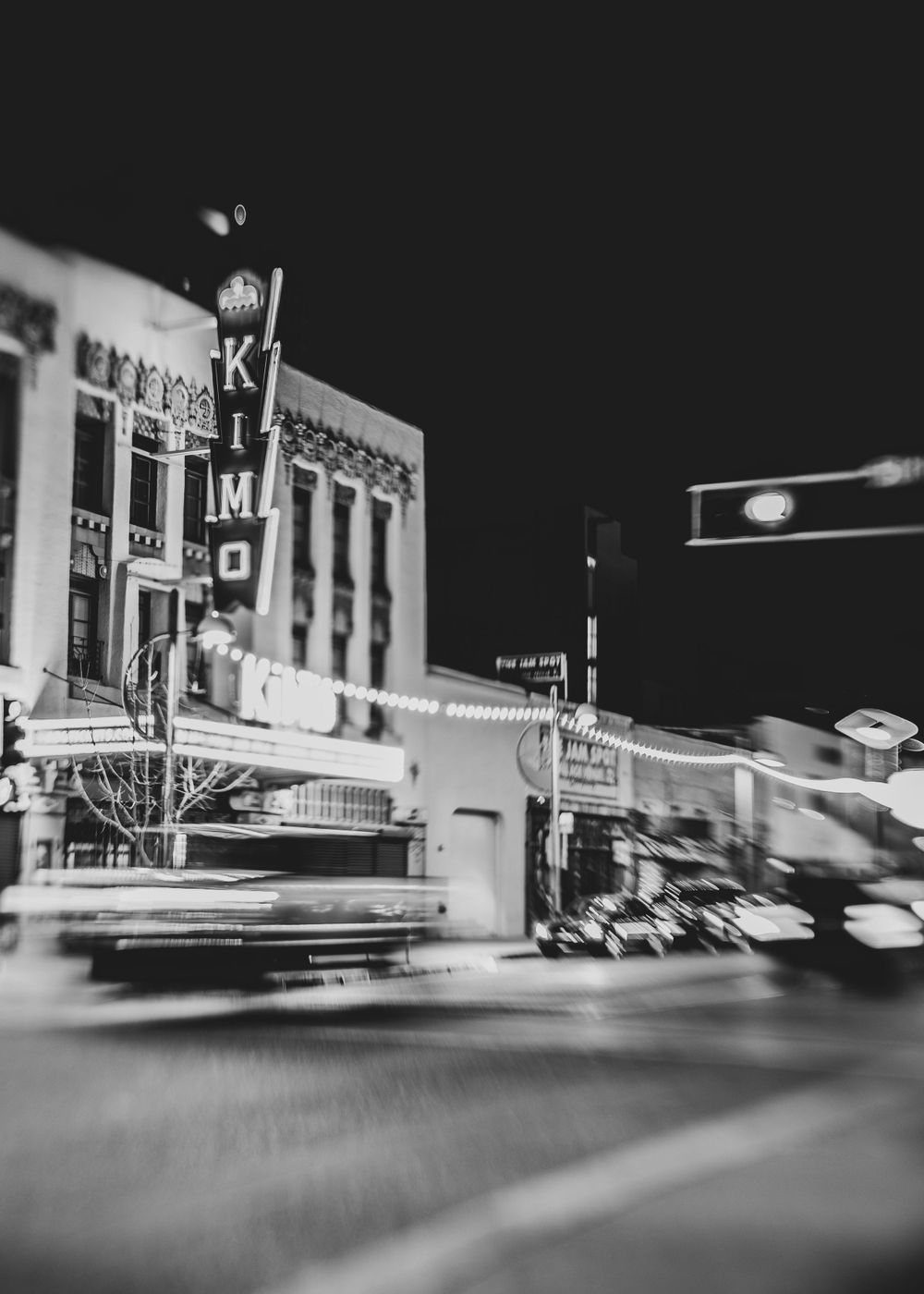 Blurred nighttime street scene with vintage Kimo theater sign in black and white.