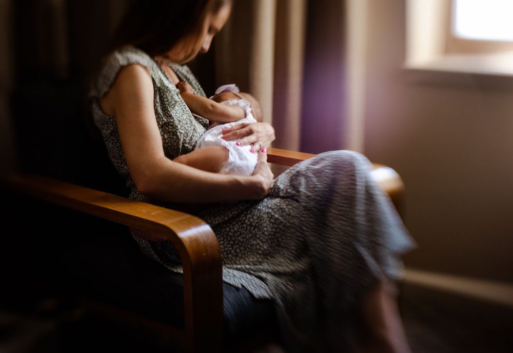 Intimate indoor portrait of someone holding a baby in soft window light.