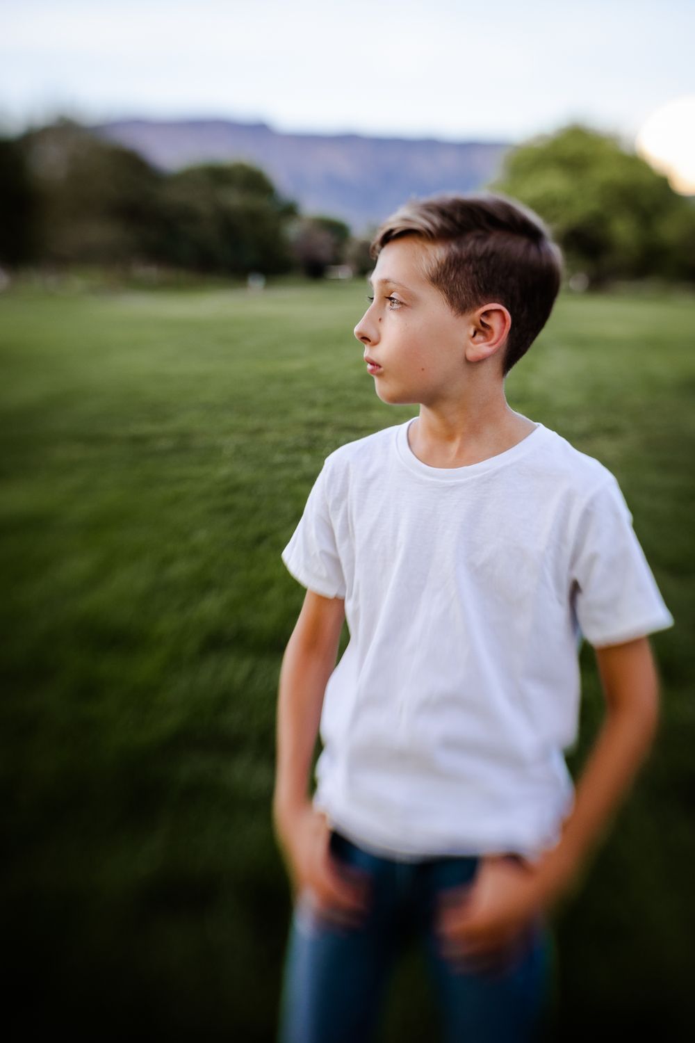 Portrait of a young person in white t-shirt standing in a grassy field with mountains in background.