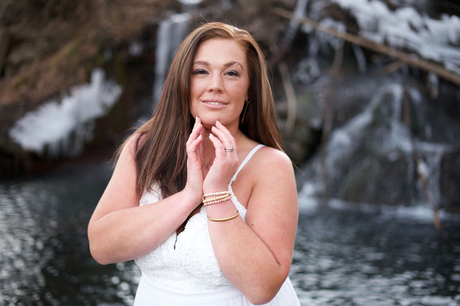 Winter portrait with snowy waterfall backdrop and white dress.