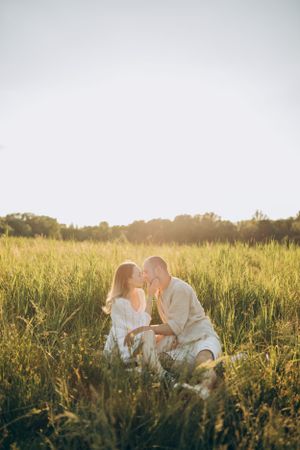 Romantic couple in white outfits share an intimate moment in a sunlit meadow during golden hour.
