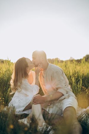 Romantic couple in white clothing share tender moment in golden field at sunset.