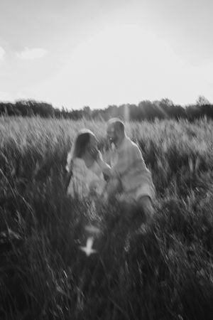 Artistic black and white capture of couple sitting in tall grass field at dusk.