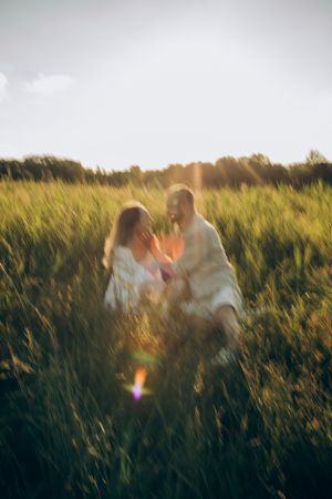 Sun flare illuminates couple in white clothing sitting together in summer meadow.