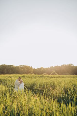 Couple in light clothing embracing in sunlit field of tall grass during sunset.