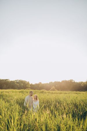 Couple stands together in green meadow during golden hour sunset.