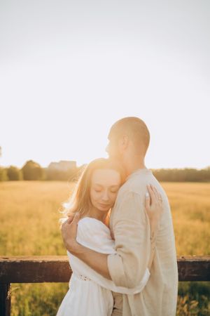Intimate moment between couple in white clothing against glowing sunset backdrop.