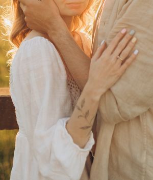 Close-up of hands and wedding ring as couple embraces in sunset light.
