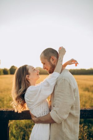 Joyful couple sharing intimate moment by wooden fence in summer field.