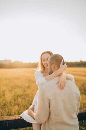 Loving embrace captured in warm sunset light against rural landscape.