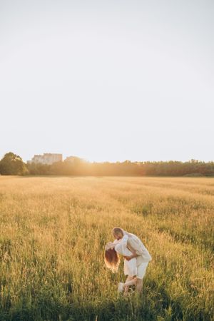 Couple in light clothing dancing in tall grass during golden hour.