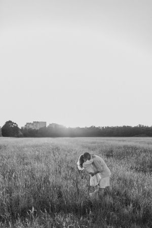 Black and white portrait of couple embracing in meadow at sunset.