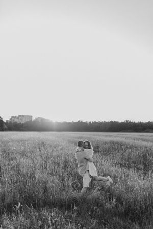 A black and white romantic moment captured in a serene meadow at sunset.