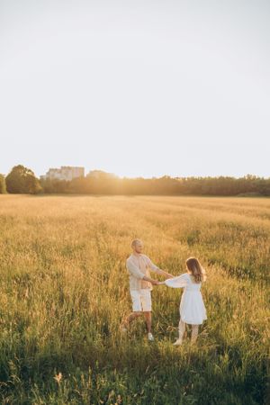 Dancing together in a sun-drenched field surrounded by golden grass at sunset.