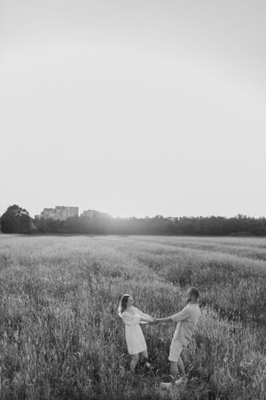 A black and white photograph of a couple dancing in an open field at dusk.