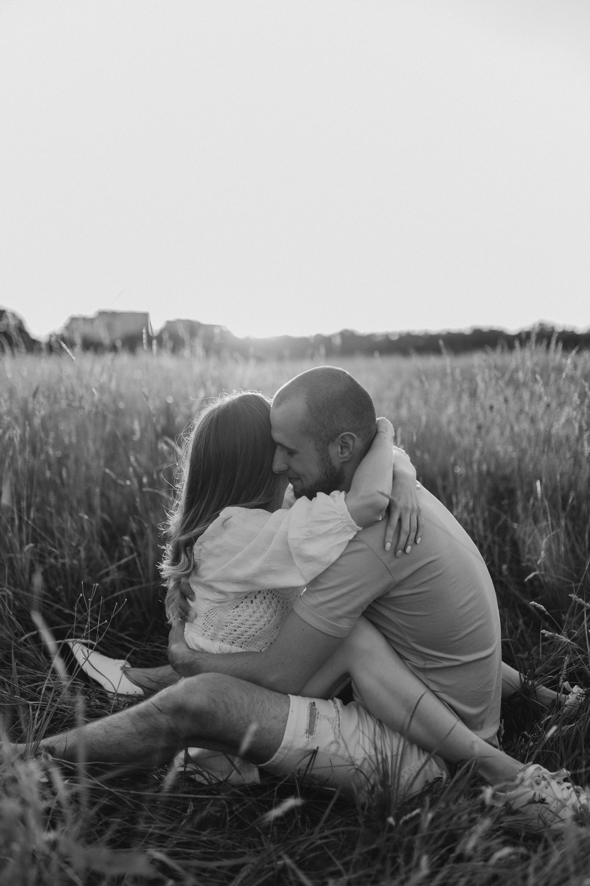 Black and white photo of couple sharing an embrace in a serene meadow.