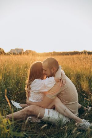 Couple embracing tenderly while sitting in tall grass during golden hour.