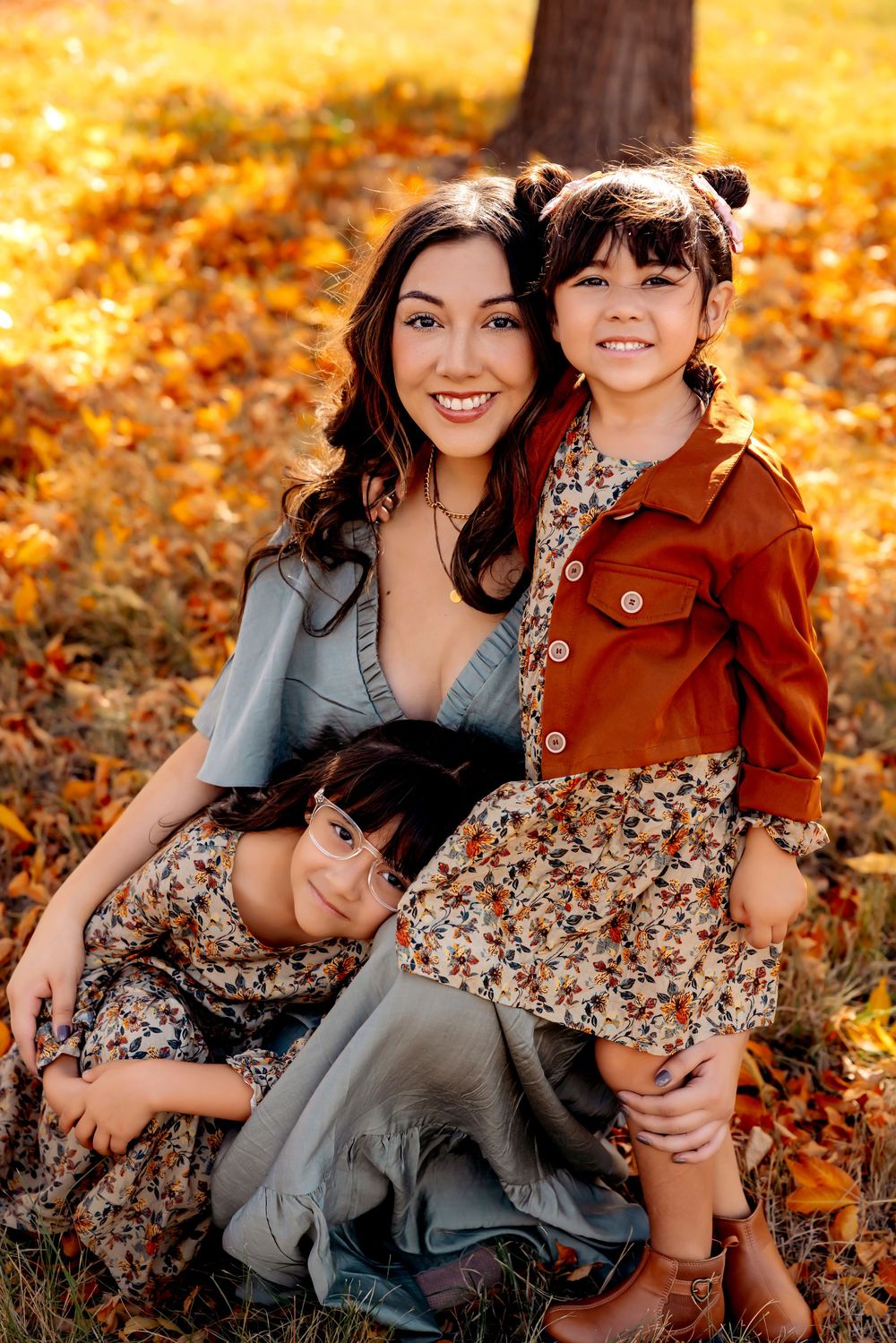 Family portrait in autumn with warm golden leaves, featuring coordinated earth-toned outfits and floral dresses.