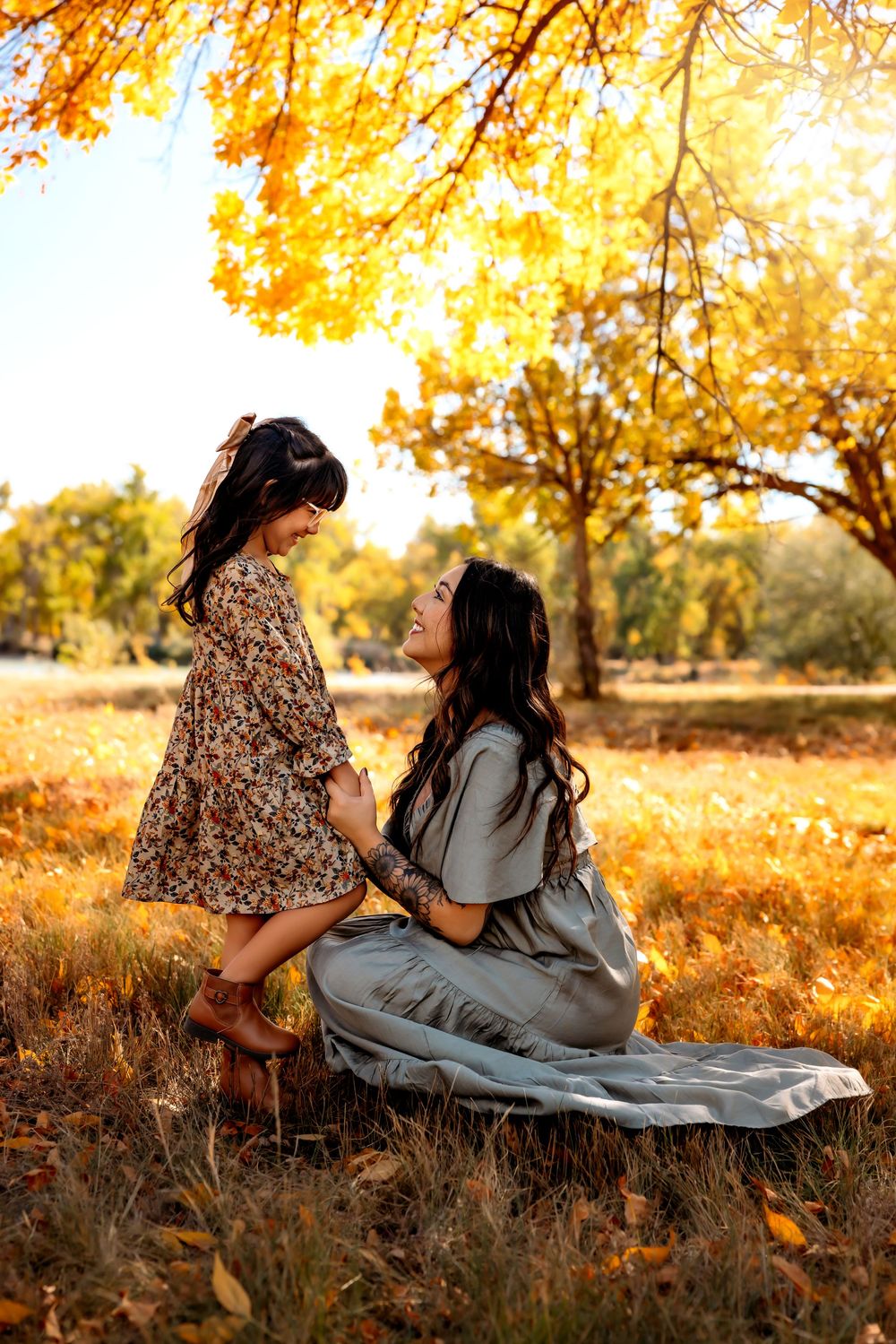 Two people in autumn attire relax on a blanket surrounded by golden fall foliage at sunset.