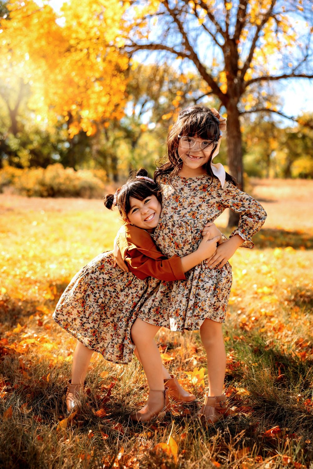 Two people play together in a field of golden autumn leaves during sunset as warm light filters through trees.