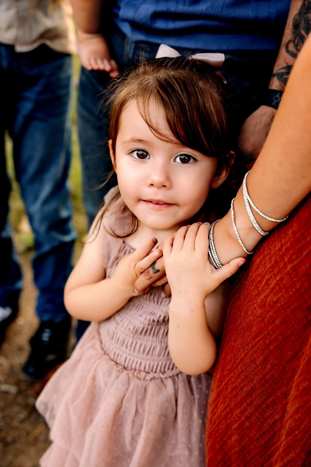 A small child in a dusty pink dress poses playfully while being held near someone wearing red.
