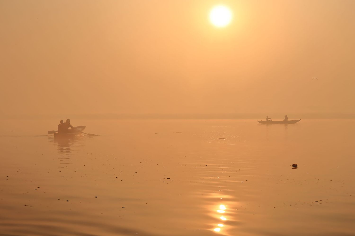 Silhouettes of boats on the Ganges River during misty golden sunrise in Varanasi.