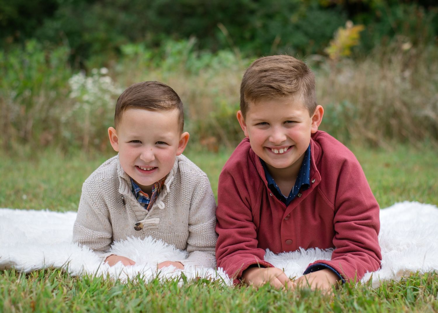 Two boys lying on white blanket outdoors smiling during autumn photo session.