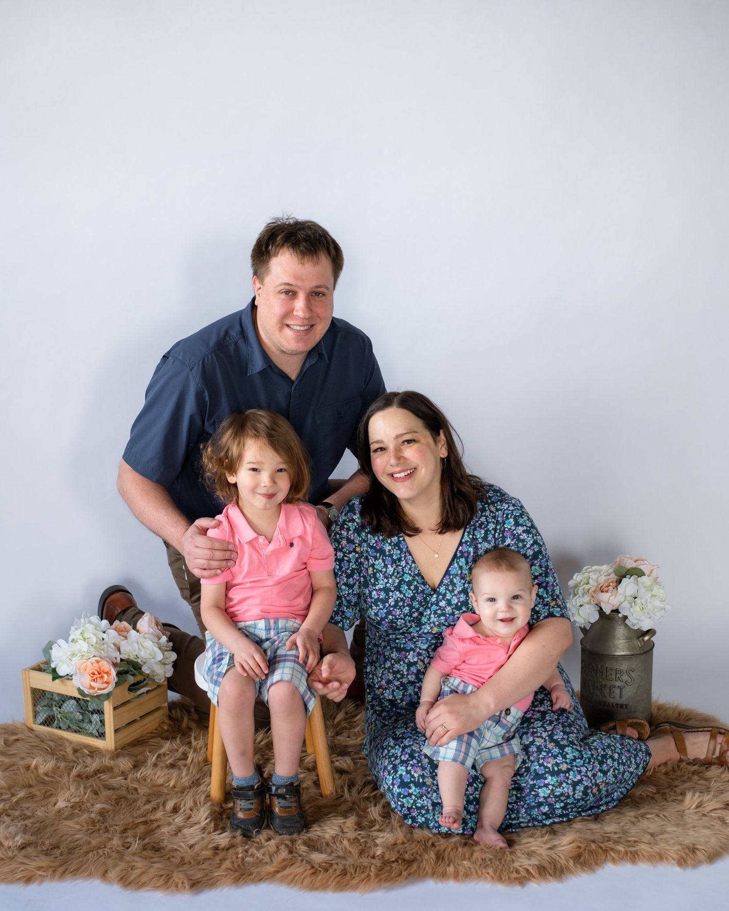 Family portrait on furry rug with vintage decor and floral arrangements.