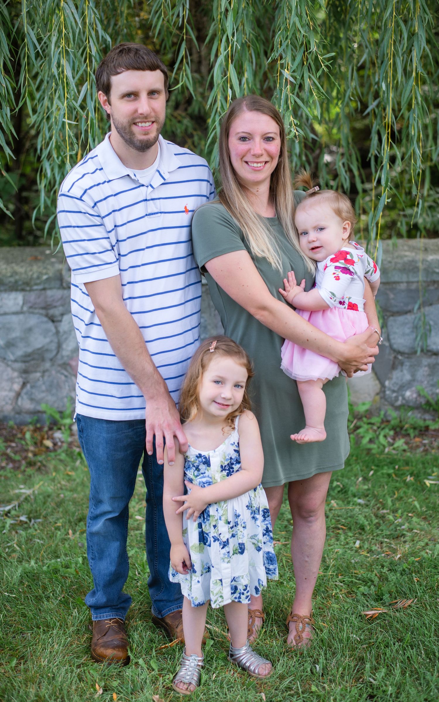 Family standing together outdoors against willow tree backdrop in summer.