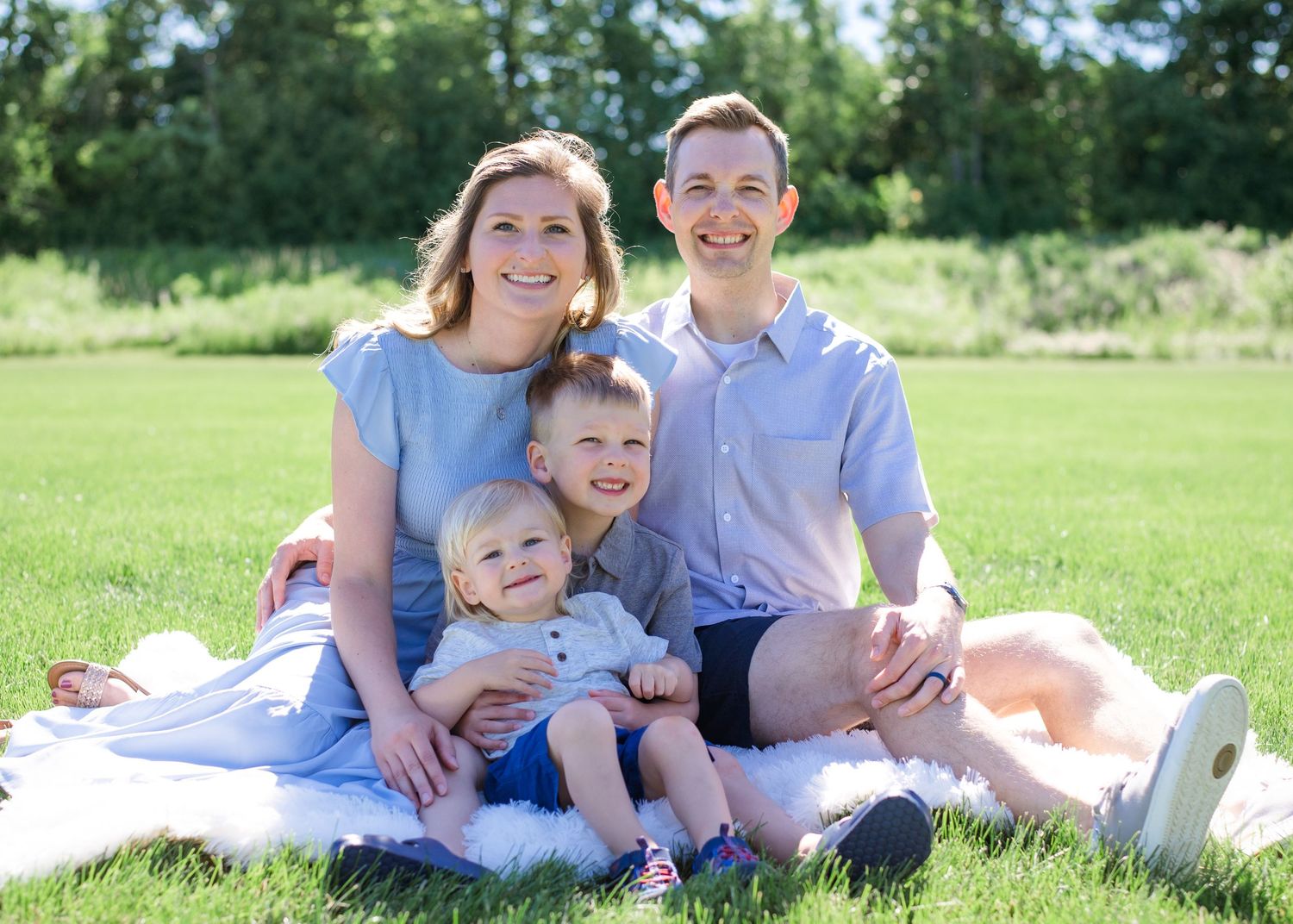 Family relaxing on picnic blanket in sunny meadow during summer photoshoot.