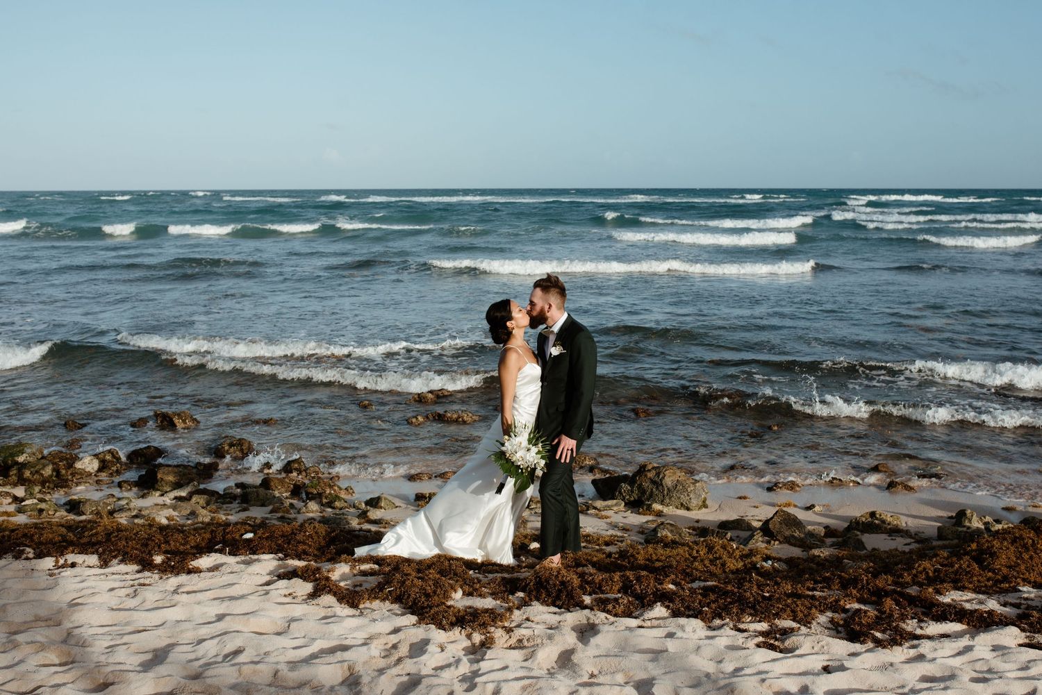 Oceanside wedding portrait with waves crashing on rocky beach in background.