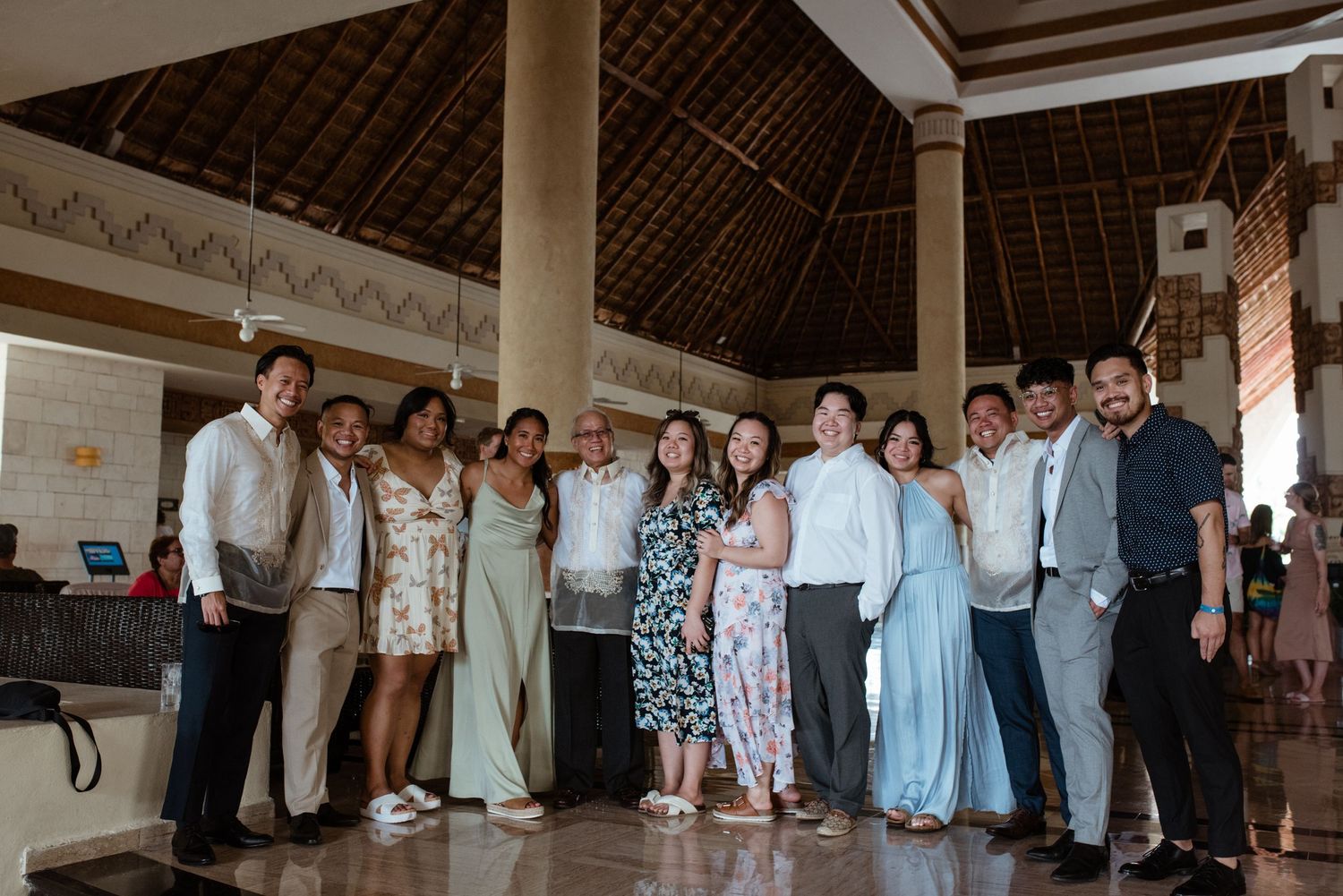 Wedding guests gather for a group photo inside a tropical resort's covered pavilion.