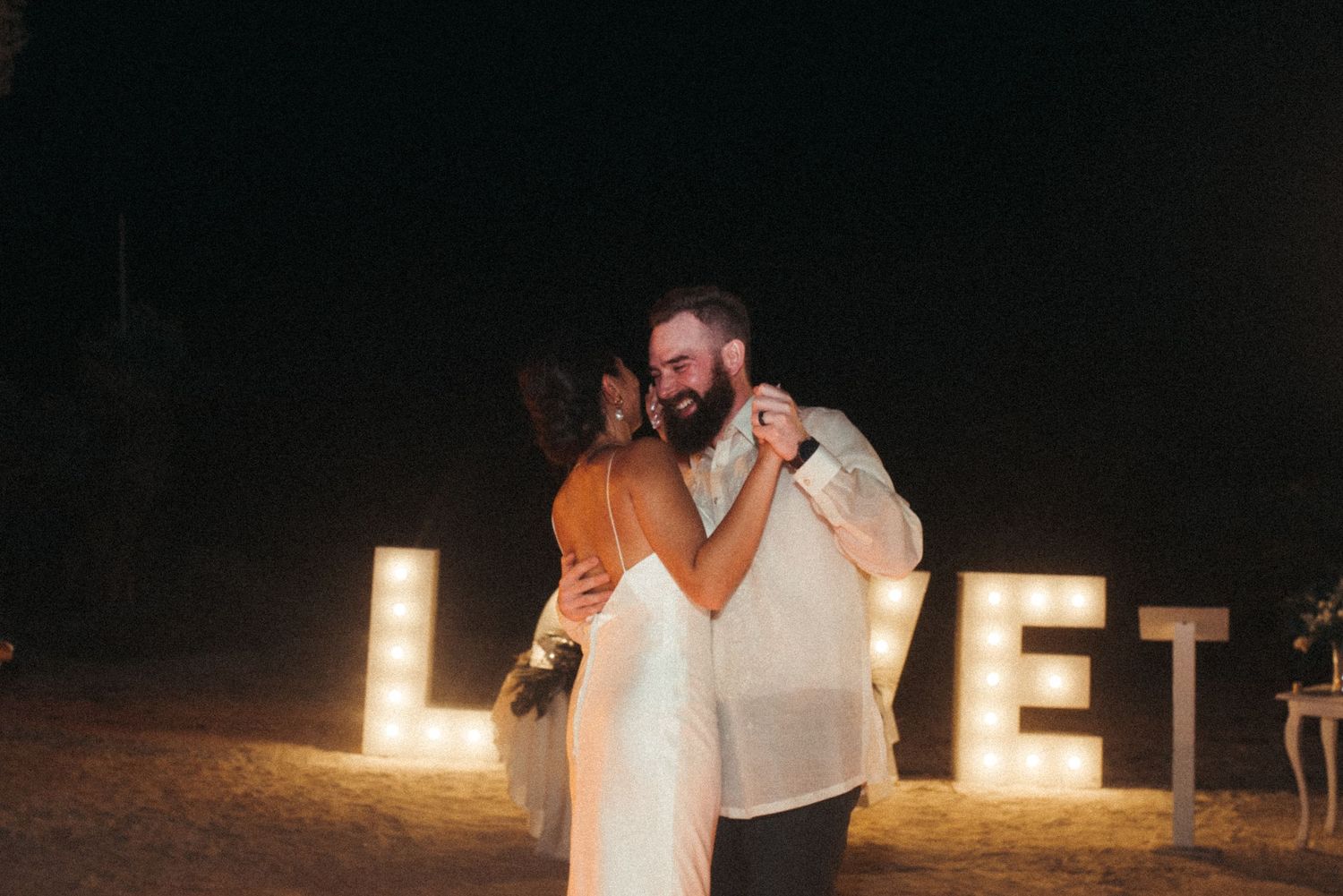 A couple dances together at night in front of illuminated 'LOVE' letters.