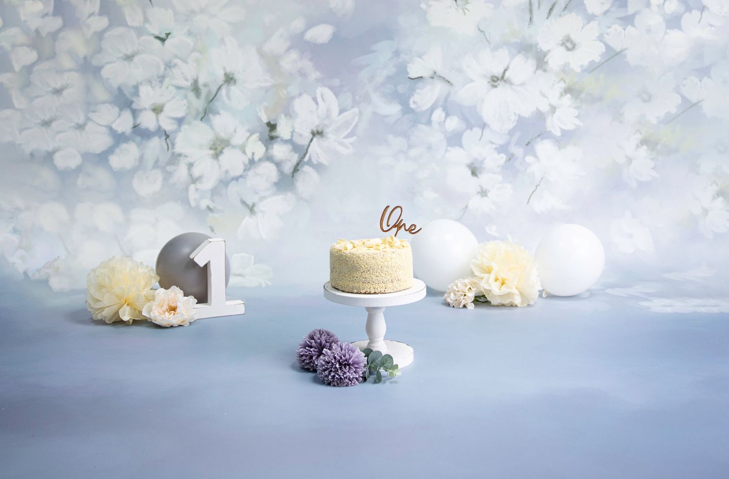 cake smash - blue/lilac/white floral backdrop white wooden cake stand, white chocolate cake with wooden 'One' topper.