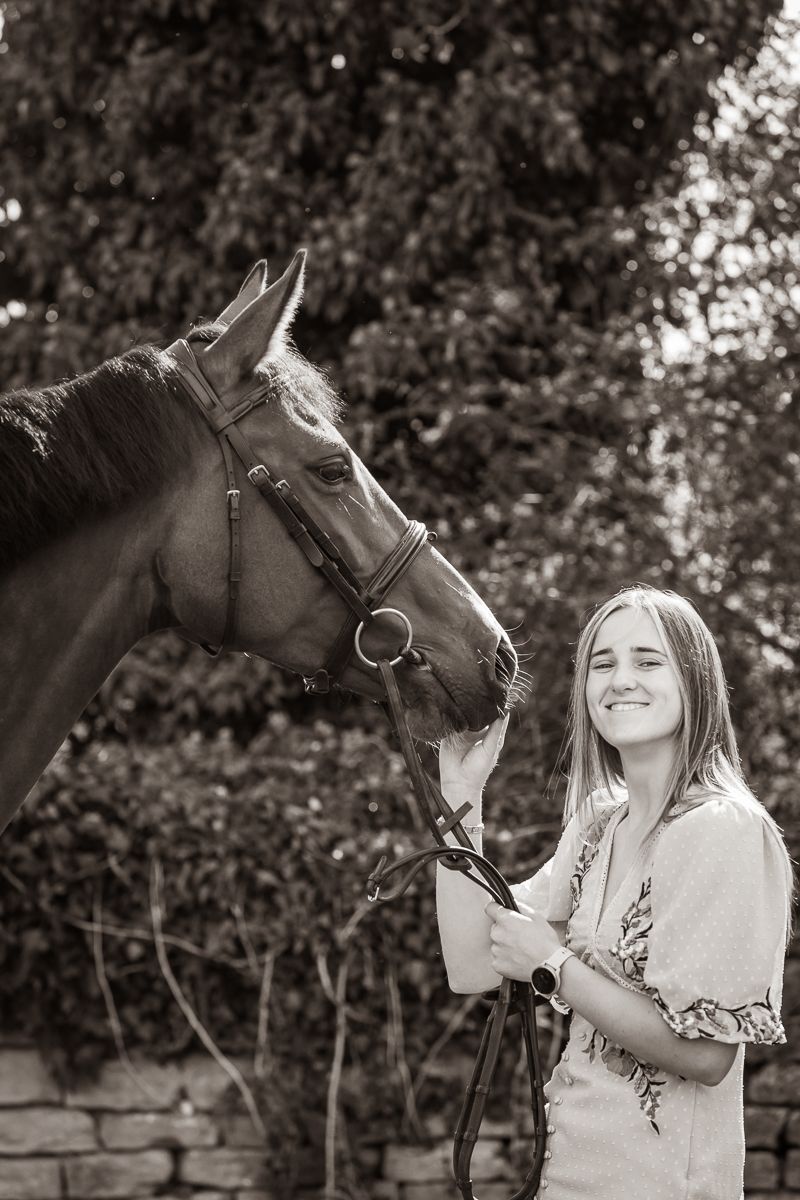 Black and white portrait showing a close moment between a horse and companion against a natural backdrop.