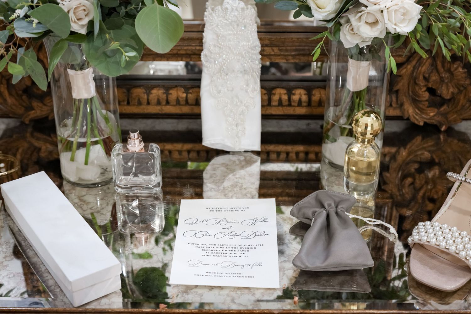 Elegant wedding details on rustic table with glass bottles, candles and calligraphy.